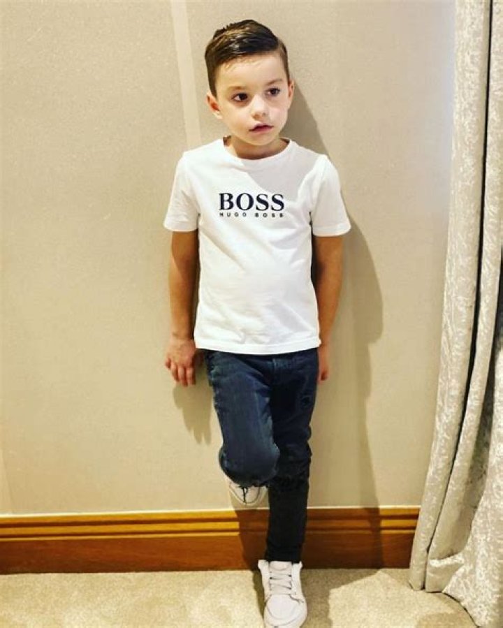 Romeo McClelland sporting a Hugo Boss T-shirt while posing with on leg on the wall behind him.